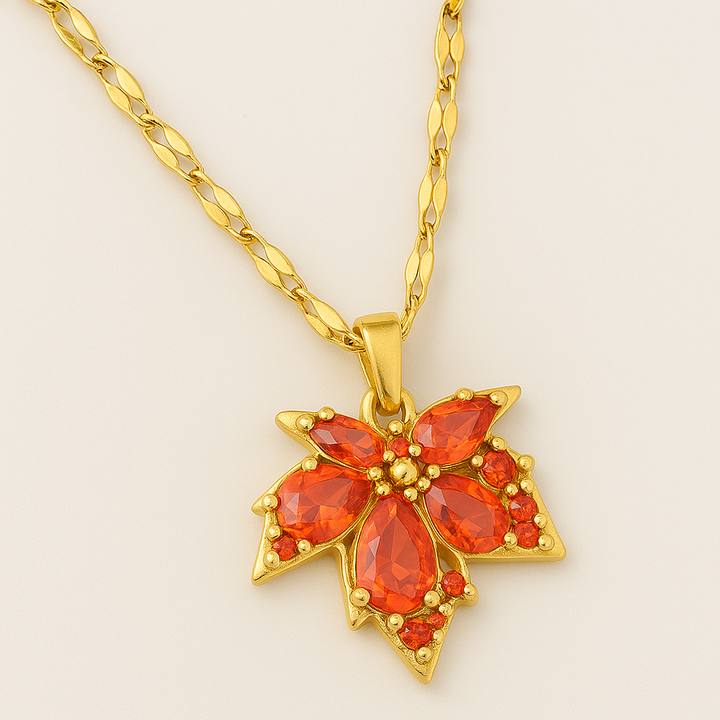 A gold-colored necklace with a radiant red gemstone maple leaf pendant.